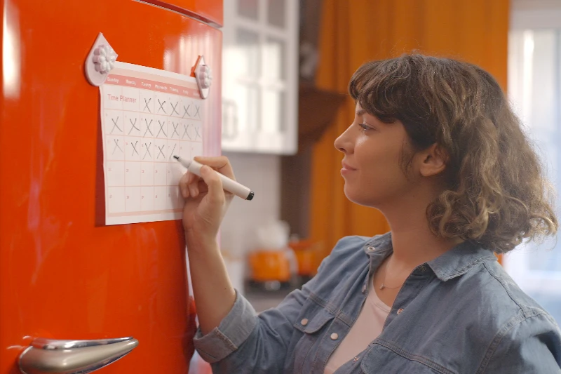 Blog 2 Woman marking off her calendar hanging on a fridge